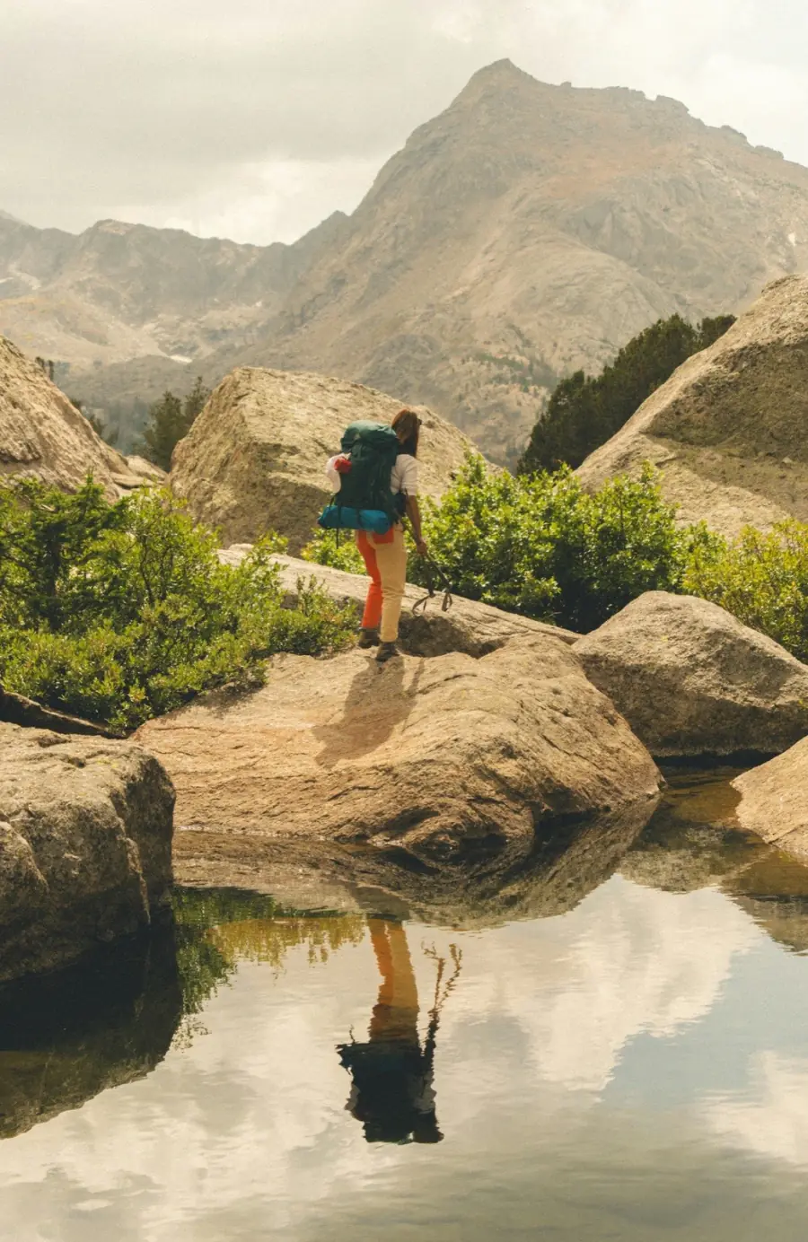 A backpacker pausing beside a still mountain lake, reflecting on the long journey ahead